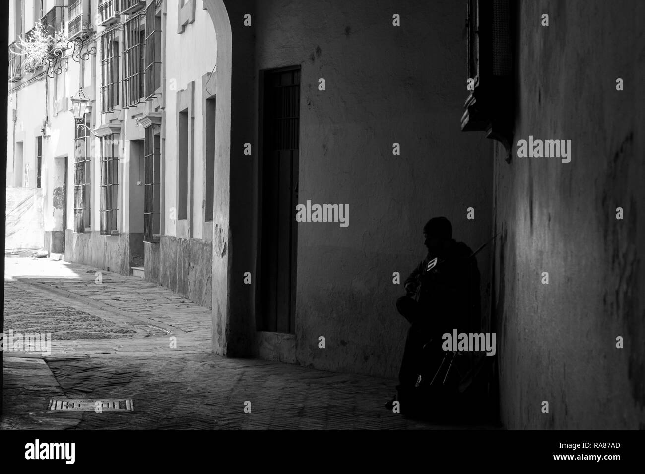 Un homme jouant de la guitare sous l'une des nombreuses arches dans les rues de la Juderia, un quartier de Séville. Photo en noir et blanc. Banque D'Images