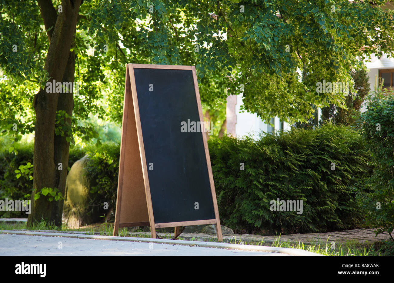 Un tableau vierge debout sur le signe de la rue, avec des plantes et des arbres autour. Banque D'Images