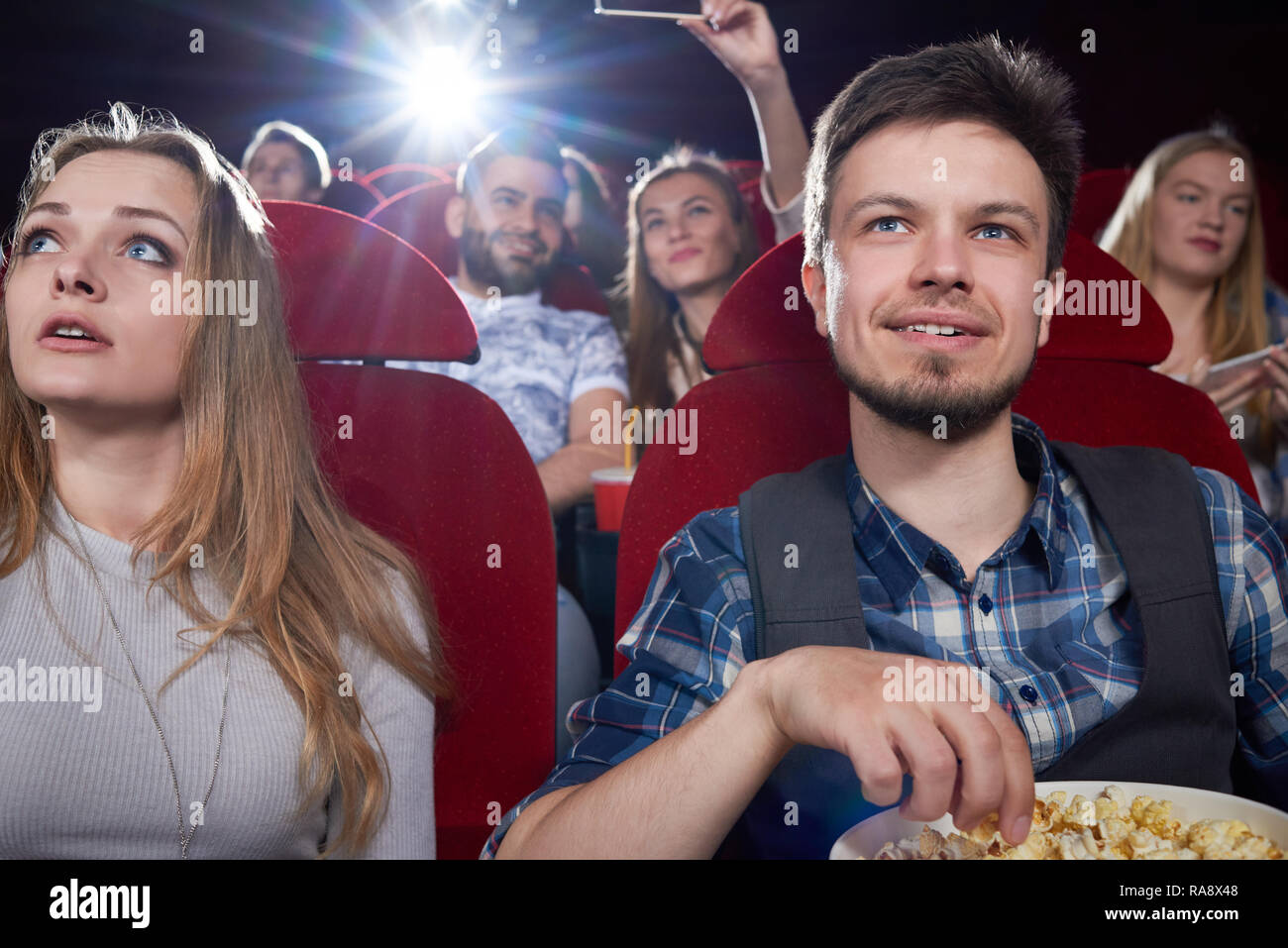 Vue avant du couple eating popcorn et à la recherche à l'écran de cinéma-théâtre avec des chaises rouges. Fille blonde en gris et bel homme romantique et profiter d'avoir date film drôle. Banque D'Images