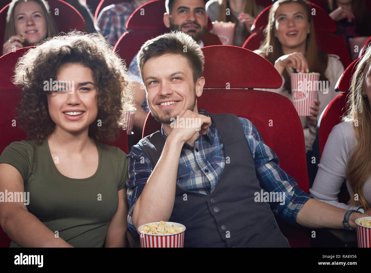 Deux amis l'homme et la fille brune assis ensemble en salle de cinéma et de sourire. Jolie petite amie et beau petit ami eating popcorn et profiter de comédie. Concept de temps libre avec des amis. Banque D'Images