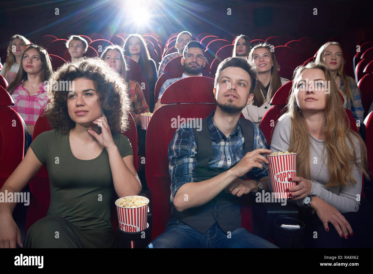 Vue de face de fille brune et de couple assis près de l'autre à étreindre et salle de cinéma. Jolie petite amie et beau petit ami eating popcorn et profiter de bon film. Banque D'Images