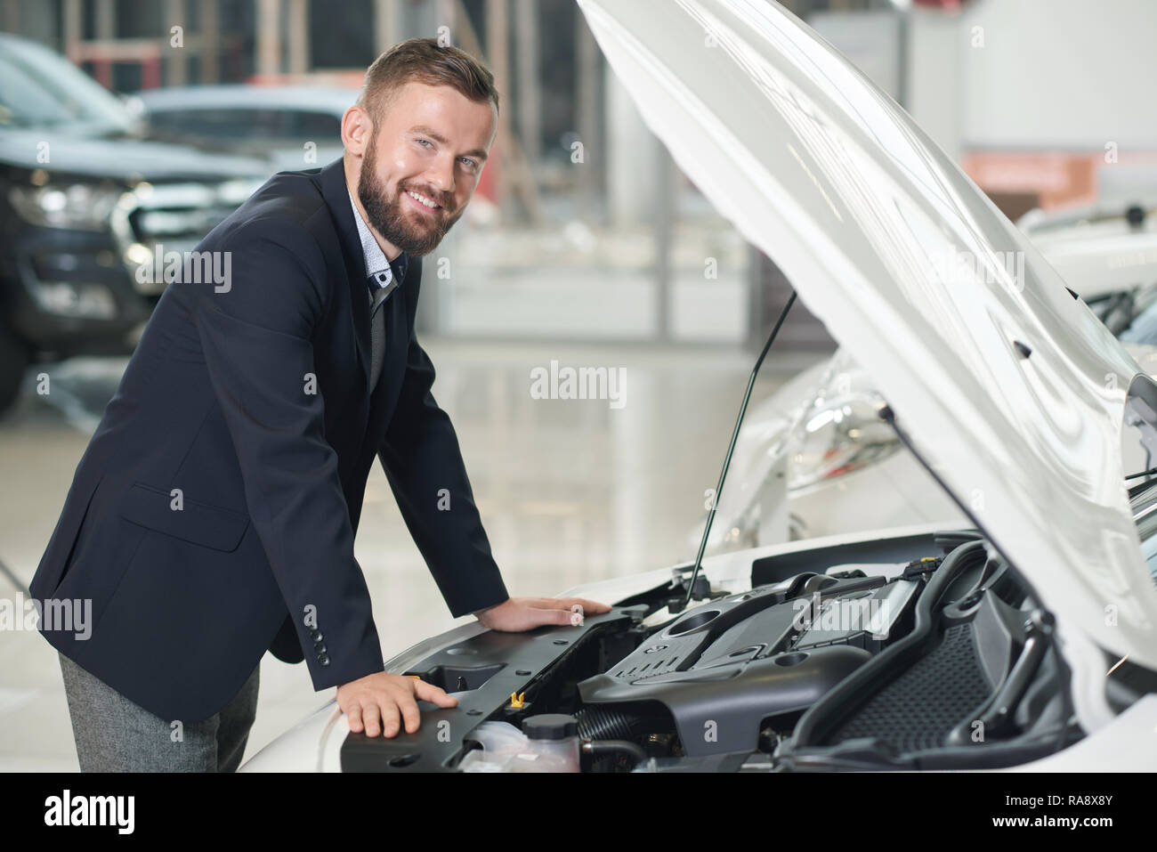 Client de l'agence de voiture s'appuyant sur voiture avec le capot ouvert. Bel homme en veste bleu foncé, smiling at camera. L'observation des clients automobiles dans le centre en voiture. Banque D'Images