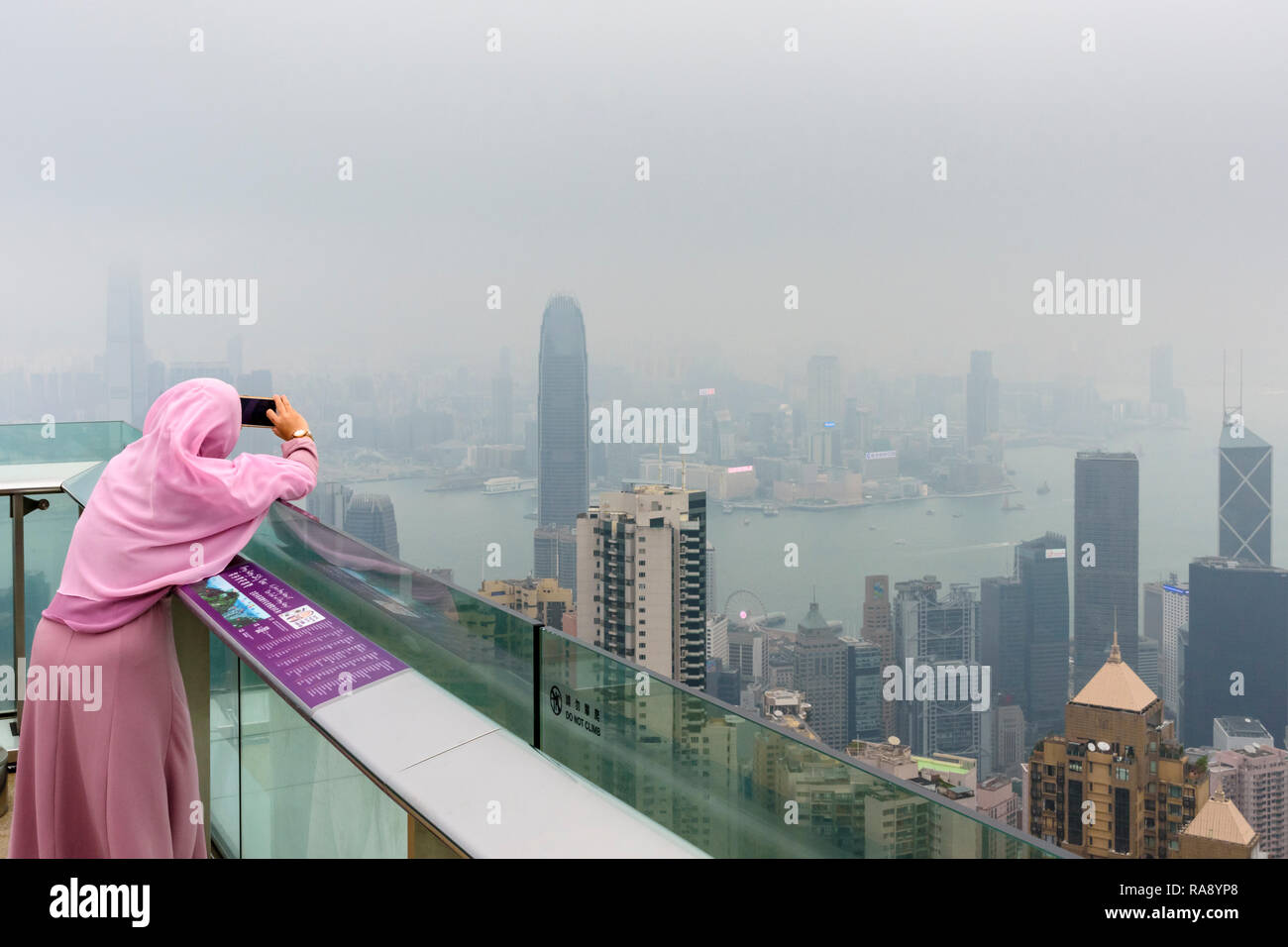 Femme prend un téléphone portable photo sur le pont de la plate-forme d'observation de la tour de pointe limitée par la brume de la pollution de l'air, Hong Kong Banque D'Images
