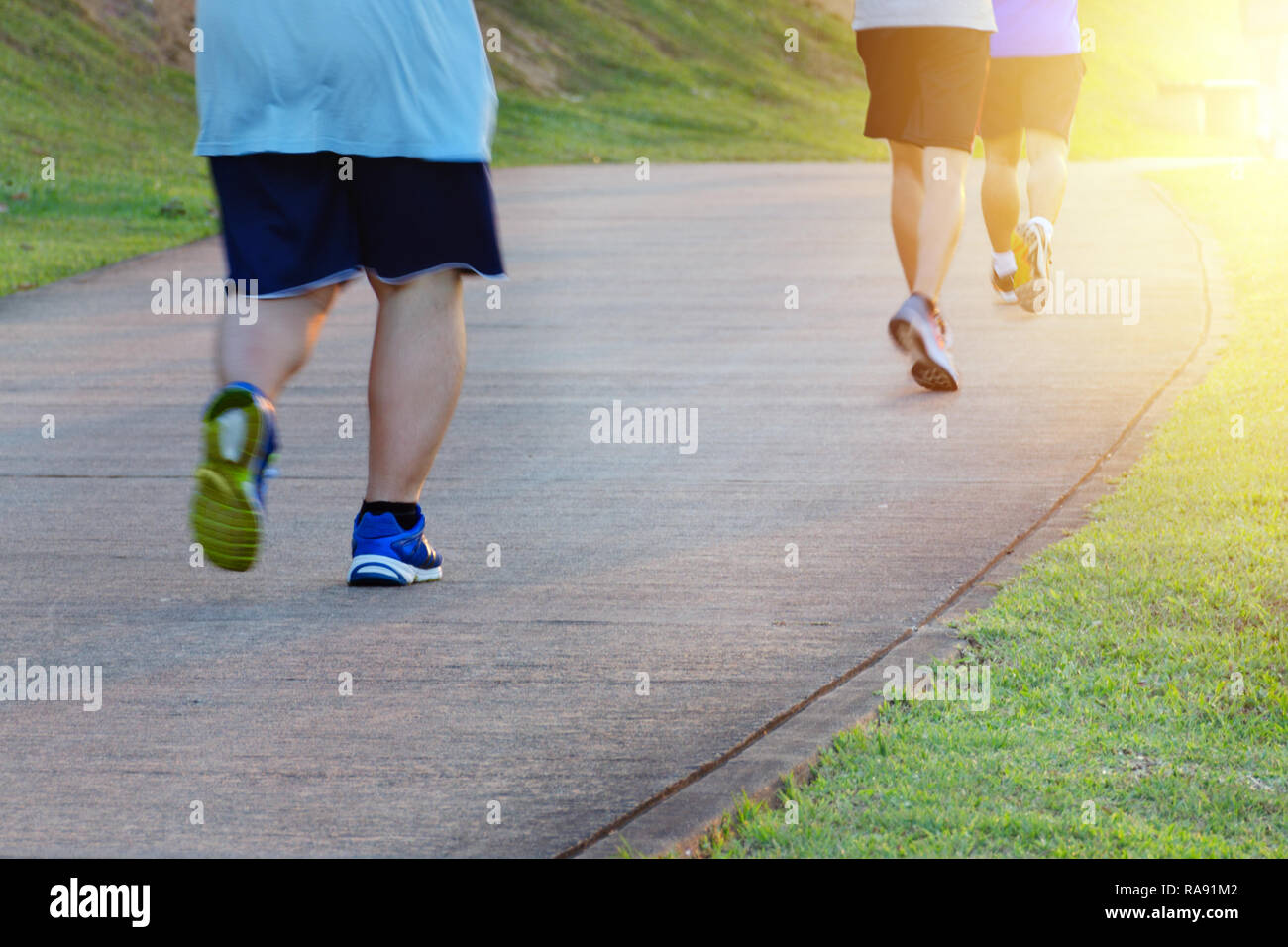 Fat Man jogging, rattraper les hommes minces. Low angle view of runners running in park. Pieds floue motion groupe de coureurs, un centre de remise en forme et en bonne santé Banque D'Images