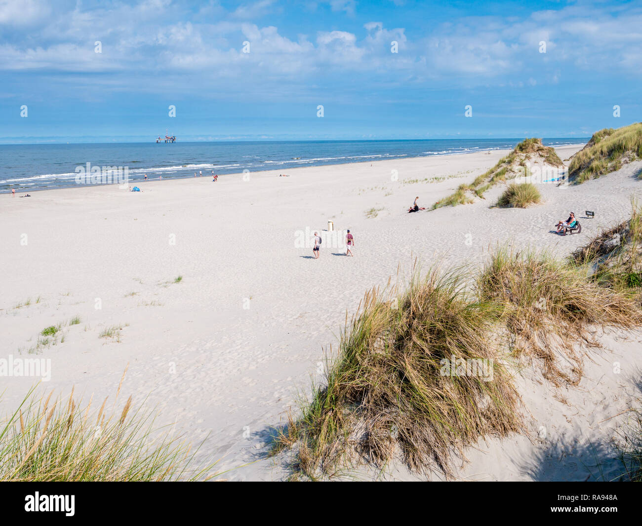 Les gens sur la plage et de la mer du Nord avec la plate-forme de forage en mer, à l'ouest de l'île de la Frise, Frise, Pays-Bas Banque D'Images