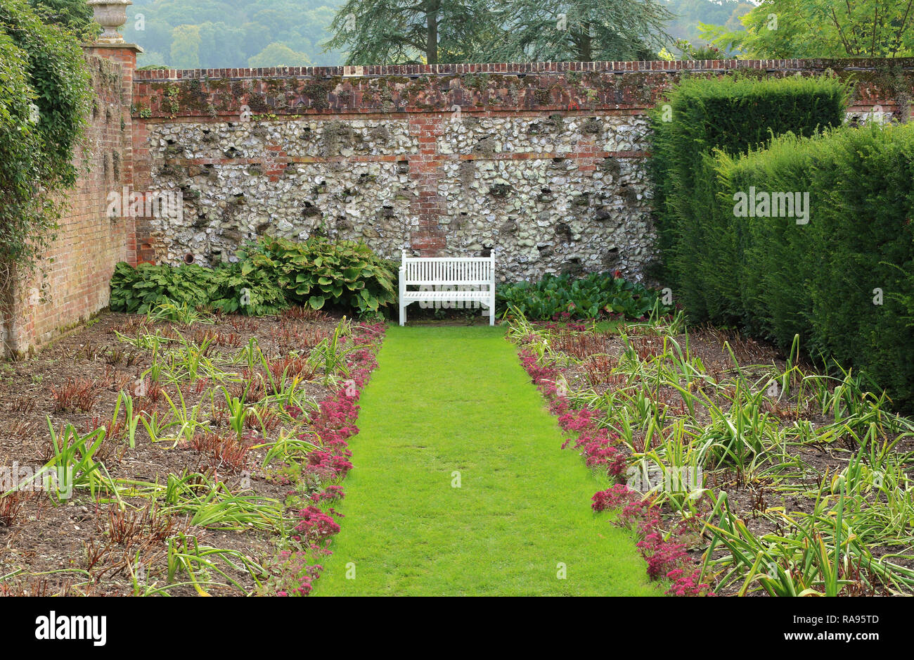 Siège de jardin en bois blanc, dans un jardin clos avec mur de briques et silex Banque D'Images