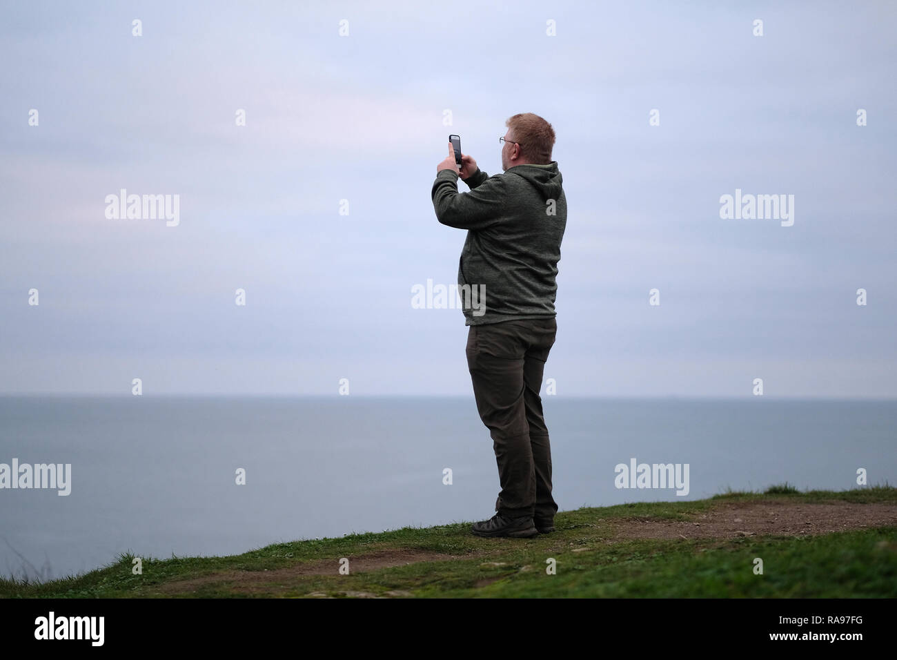 Un homme sur une colline au bord de la mer prendre un en selfies Cornwall, UK. Banque D'Images
