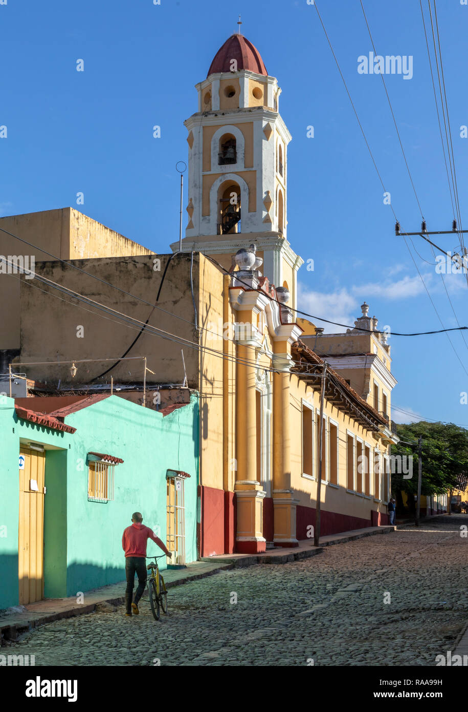 Homme marchant le long de la Calle vélos Boca ci-dessous beffroi de l'ancien couvent San Francisco, Trinidad, Cuba Banque D'Images