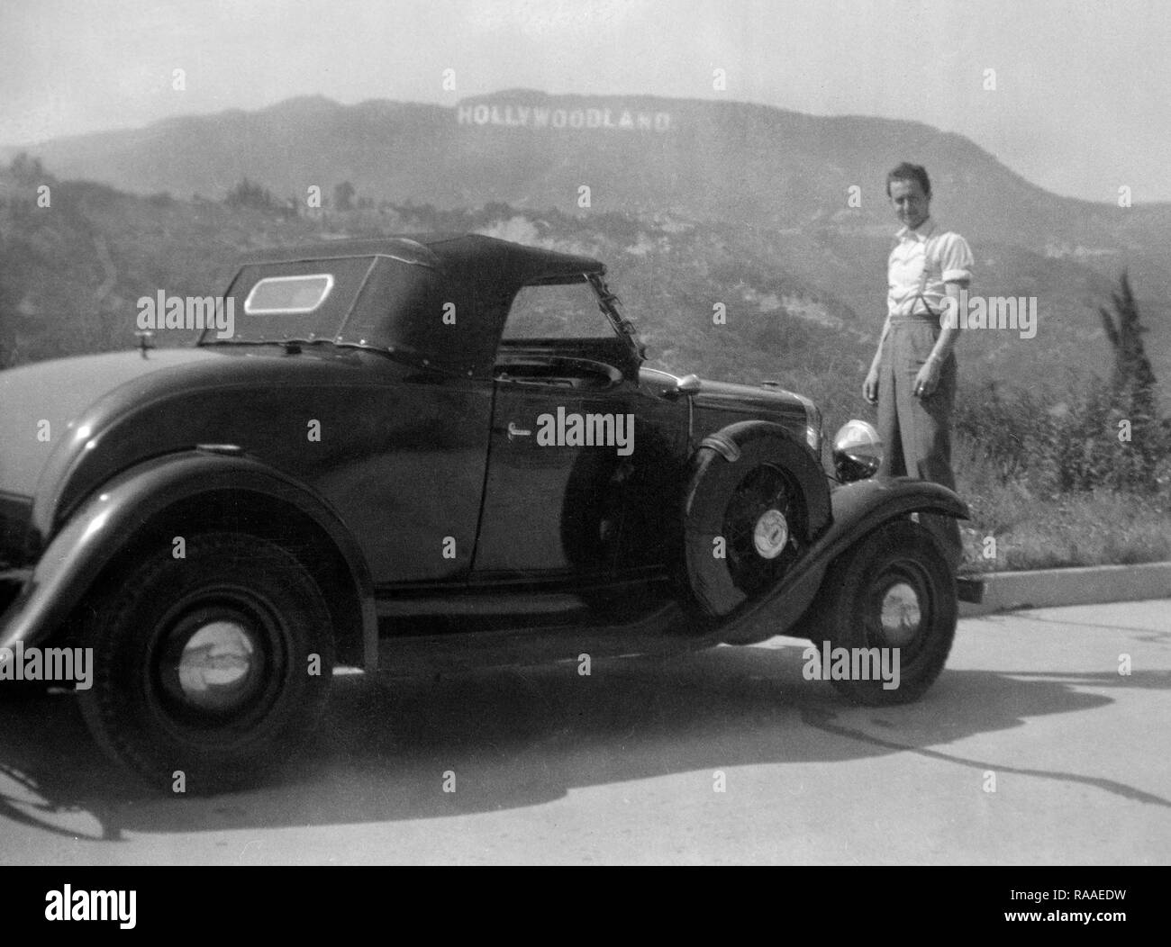 Un jeune homme pose avec sa voiture avec l'original Hollywoodland signe, ca. L'année 1930. Banque D'Images