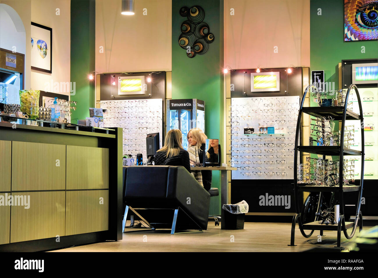 Client et de l'optométriste à l'oeil ; magasin de verre blonde female customer shopping pour lunettes d'être aidé par blonde commis de magasin. Banque D'Images