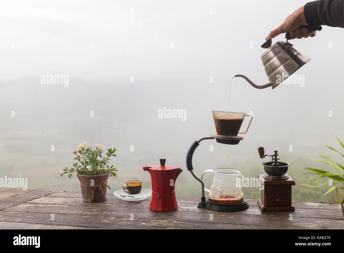 Tasse de café du matin avec le Rotary rectifieuse de café et pot de fleurs sur la table en bois avec vue sur la mer de brouillard arrière-plan, image avec copie espace. Banque D'Images