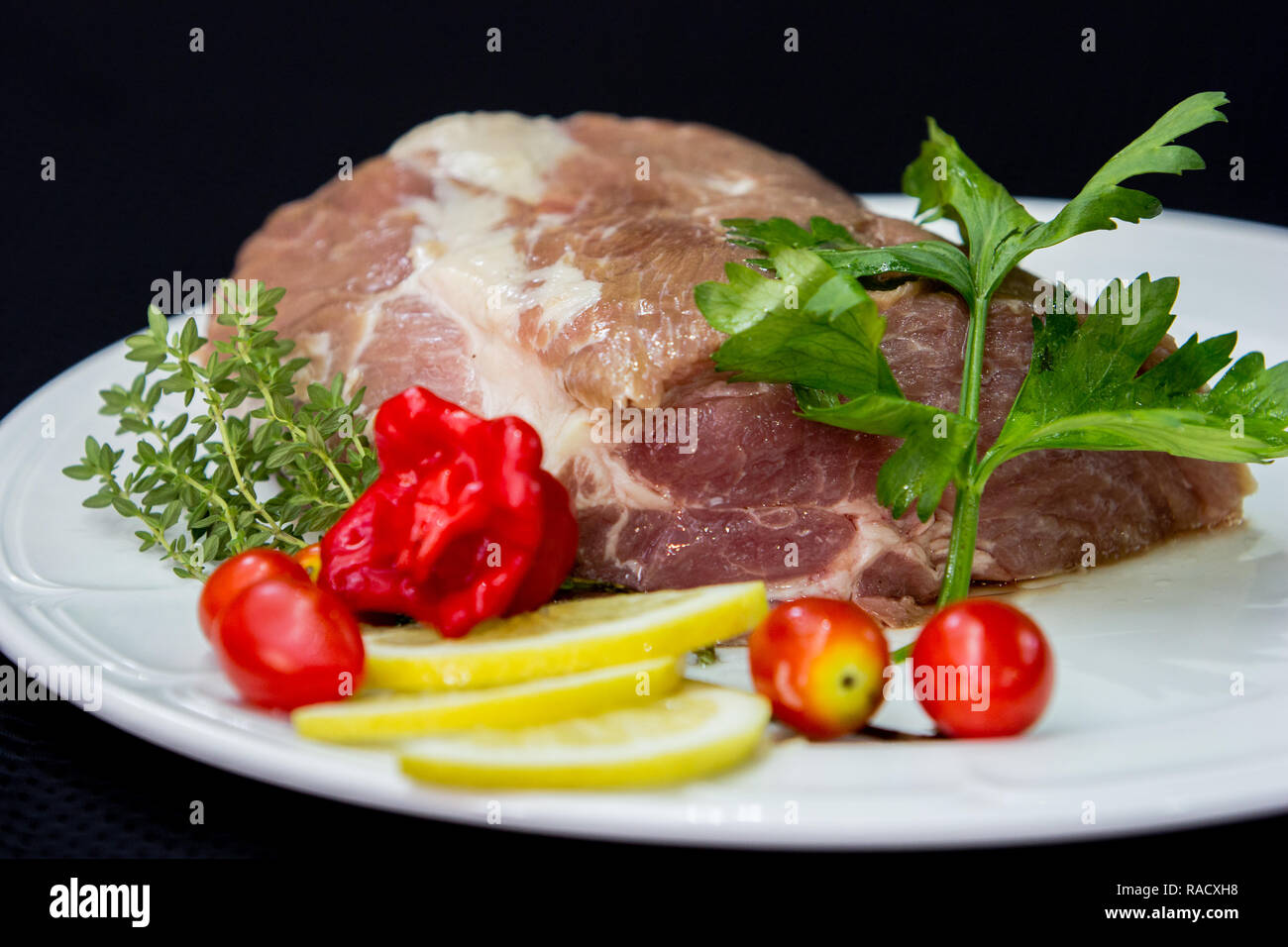 La viande de buffle crus crus prêts à cuire dans une plaque blanche avec des tomates, du citron et des herbes d'un fond noir. Banque D'Images