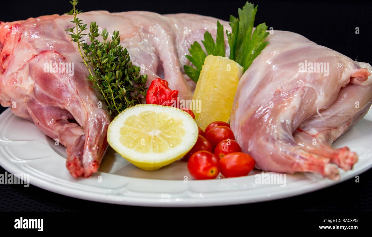 Les viandes de lapin aux herbes et d'épices sur une plaque blanche sur un fond noir prêt à cuire. Banque D'Images