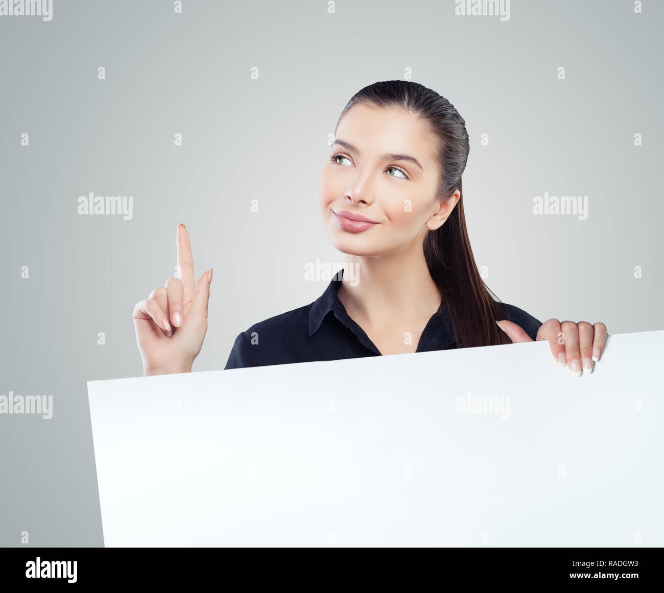 Smiling businesswoman pointing up et montrant le papier vide pancarte avec espace salon exemplaire vierge pour slogan, advertisiment ou message texte sur le dos gris Banque D'Images