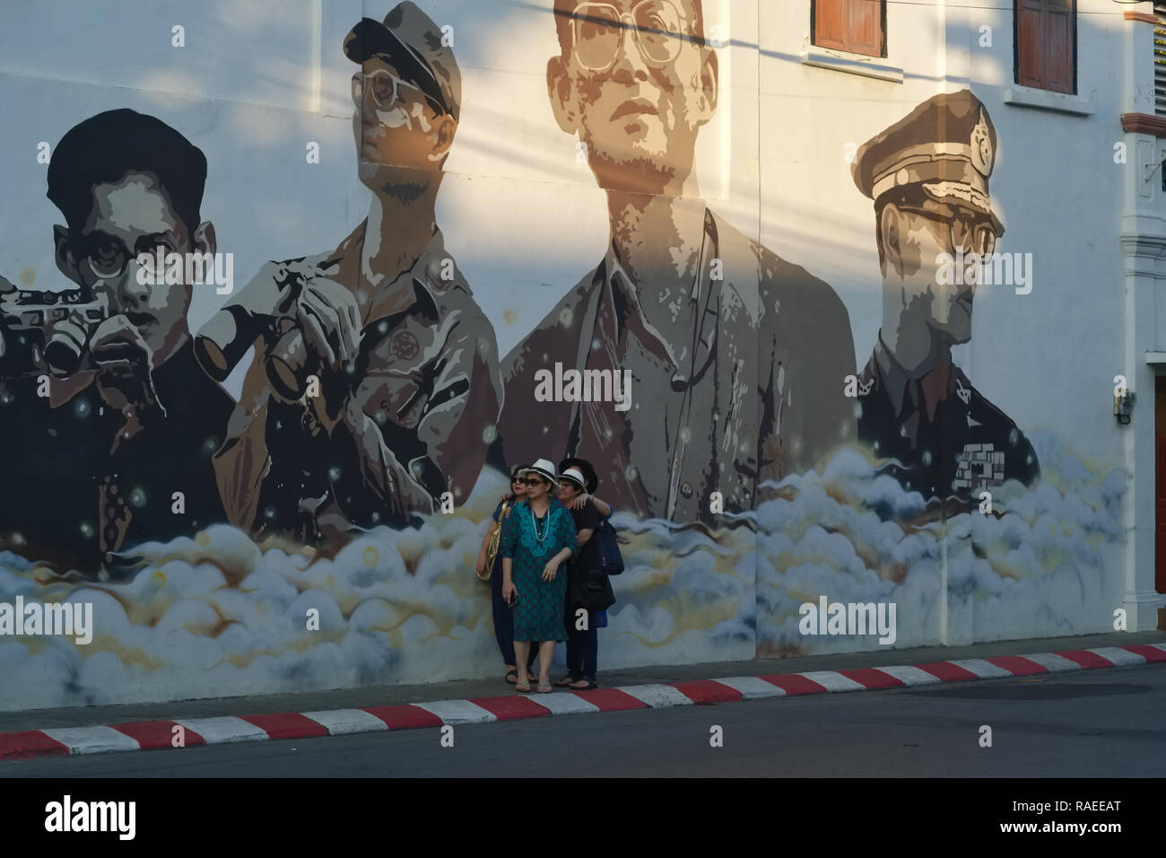 Les touristes dans la ville de Phuket, Thaïlande, posent le cadre d'une peinture murale représentant l'ancien Roi Bhumipol Adulyadej dans différentes phases de sa vie Banque D'Images