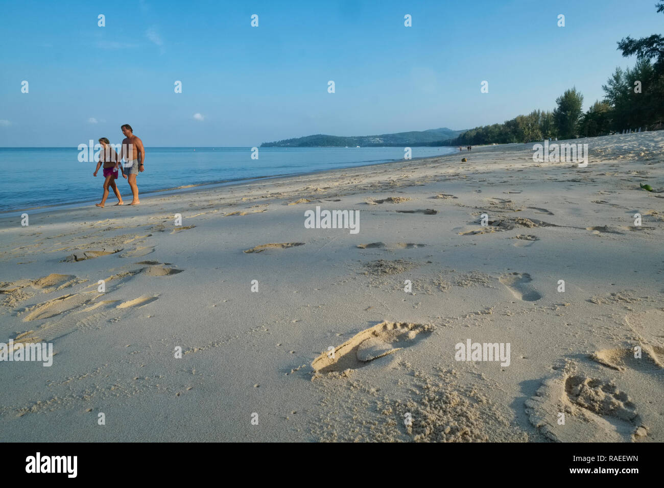 Un couple sur une promenade tôt le matin à Bang Tao Beach, Phuket, Thaïlande ; à l'avant-plan des traces de pas dans le sable Banque D'Images