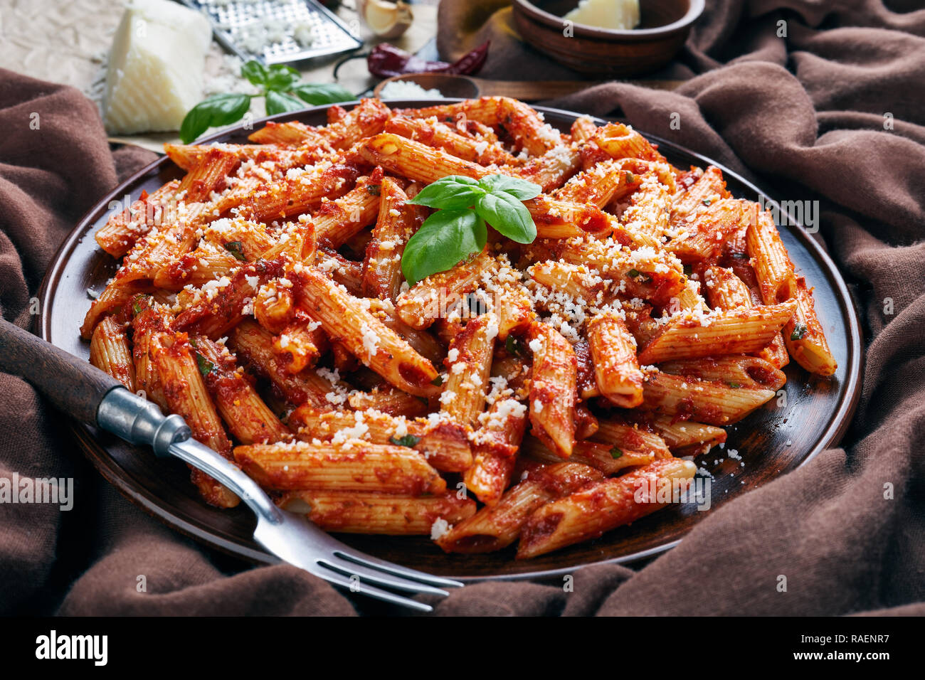 Close-up de style classique italien avec l'arrabiata penne sauce tomate chaude sur une plaque d'argile avec le basilic et le fromage de chèvre râpé sur une table rustique avec brown Banque D'Images