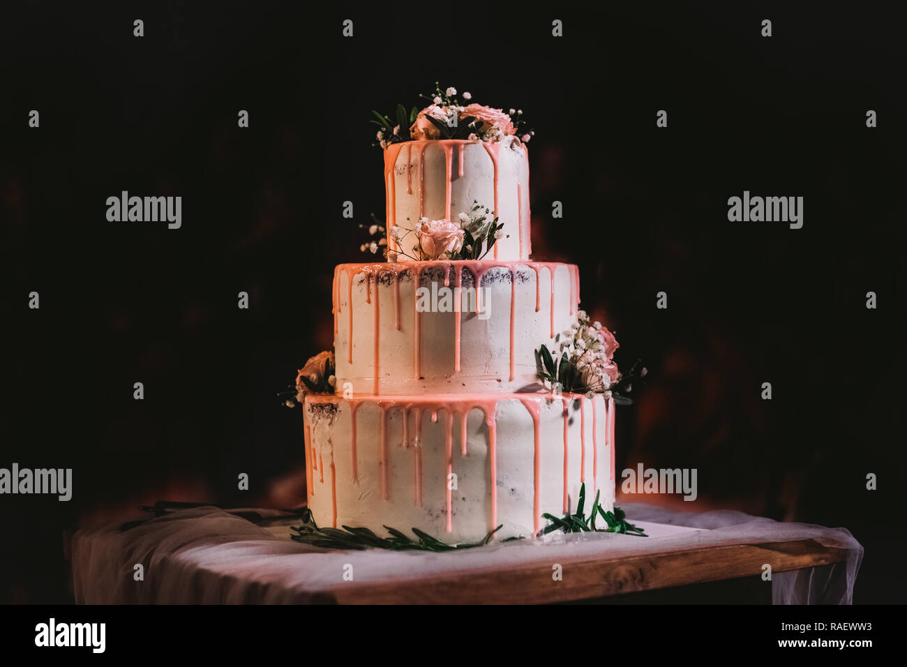 Elegant big belle trois couches gâteau de mariage décoré blanc crème et rose avec des fleurs fraîches. Comité permanent sur la table gâteau isolée à fond noir Banque D'Images