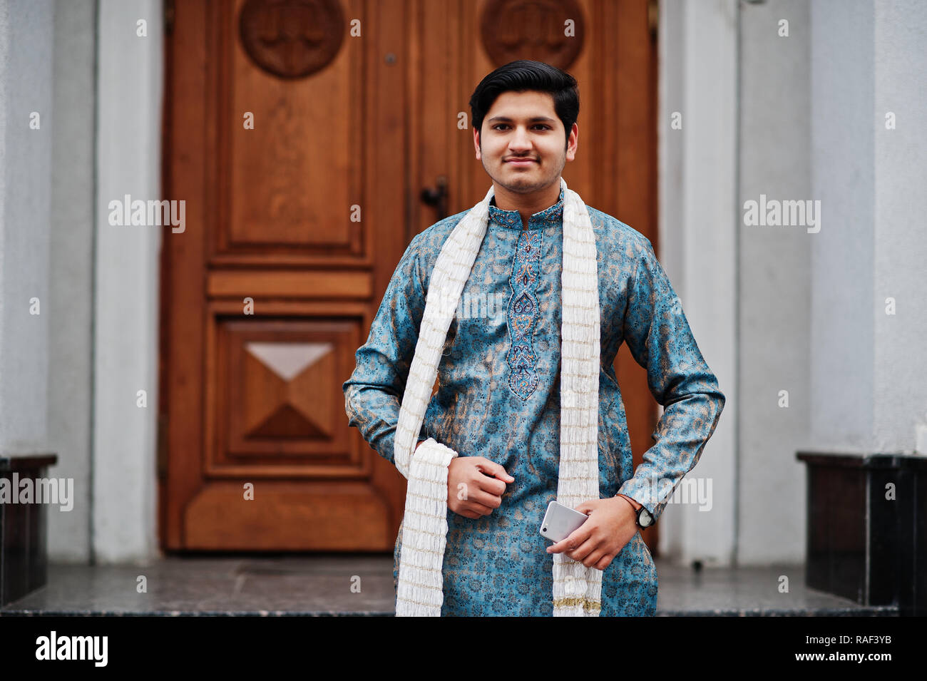 L'homme indien l'usure des vêtements traditionnels avec l'écharpe blanche  posée contre une porte de bâtiment avec téléphone portable à la main Photo  Stock - Alamy