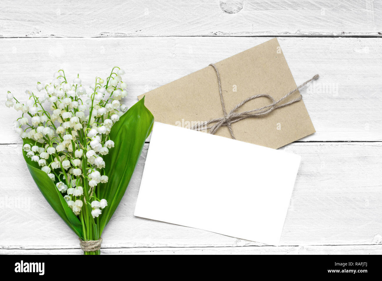 Blanc Blanc carte de vœux et enveloppe avec printemps muguet fleurs. valentines ou womens day background. Vue de dessus la maquette. Banque D'Images