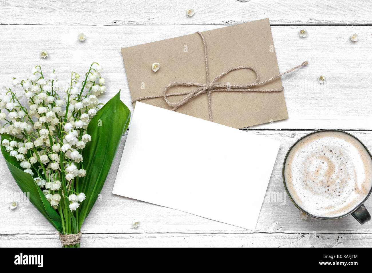 Blanc Blanc carte de vœux et enveloppe avec printemps muguet fleurs et tasse de Cappuccino. valentines ou womens day background. vue d'en haut. mo Banque D'Images