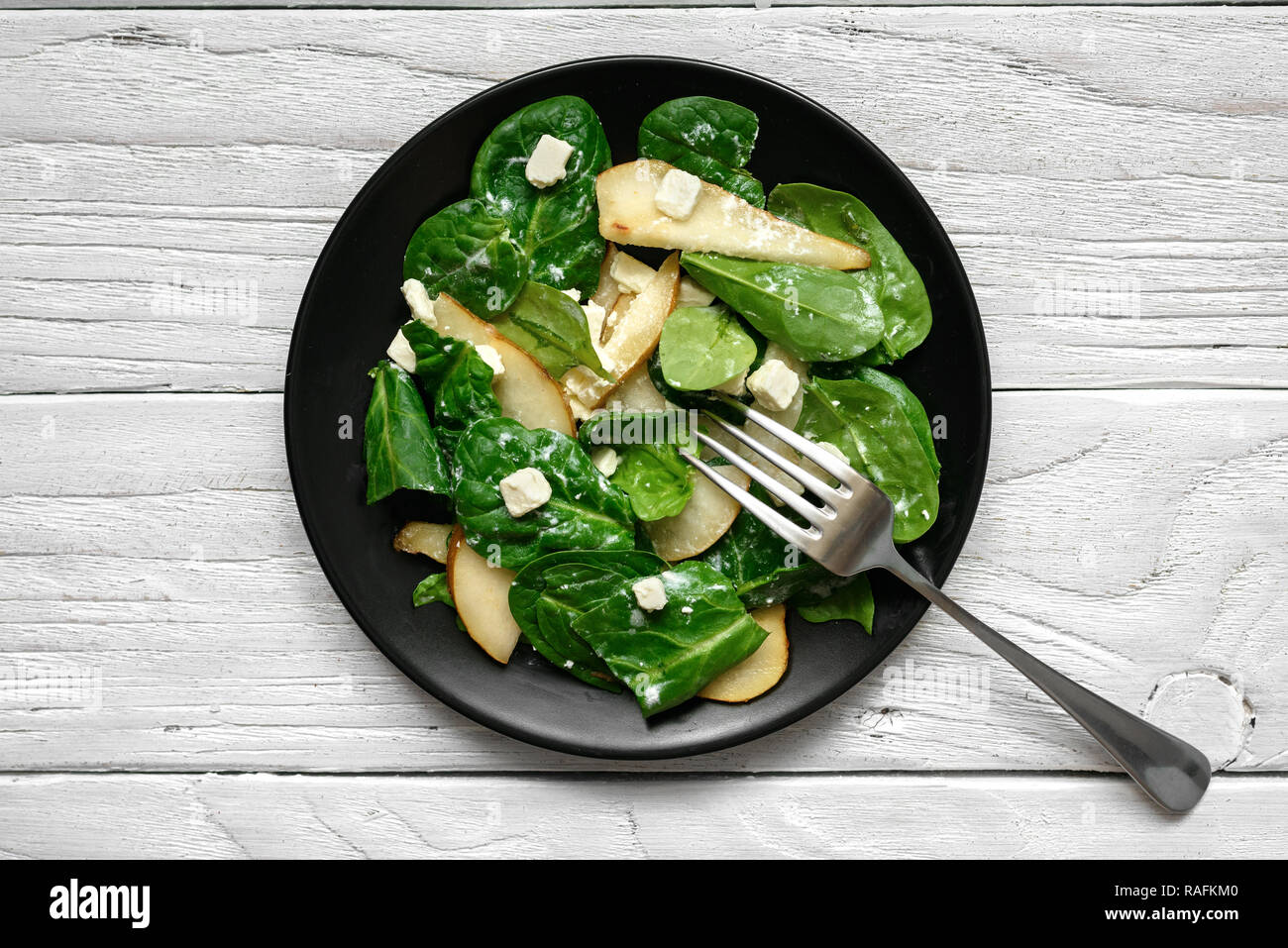 Salade avec les feuilles d'épinards, poire et fromage feta avec fourchette en plaque noire. La nourriture végétarienne saine. Vue de dessus Banque D'Images