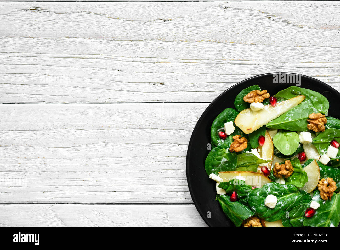 Salade avec les feuilles d'épinards, de poire, de noix, de grenade et le fromage feta en plaque noire. La nourriture végétarienne saine. top view with copy space Banque D'Images