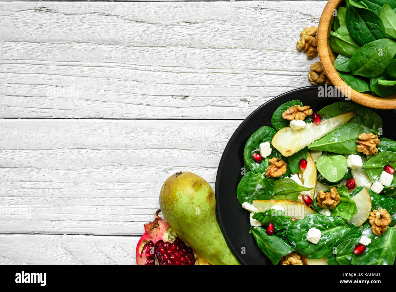 Salade vitamine avec les feuilles d'épinards, de poire, de noix, de grenade et le fromage feta en plaque noire. La nourriture végétarienne saine. top view with copy space Banque D'Images