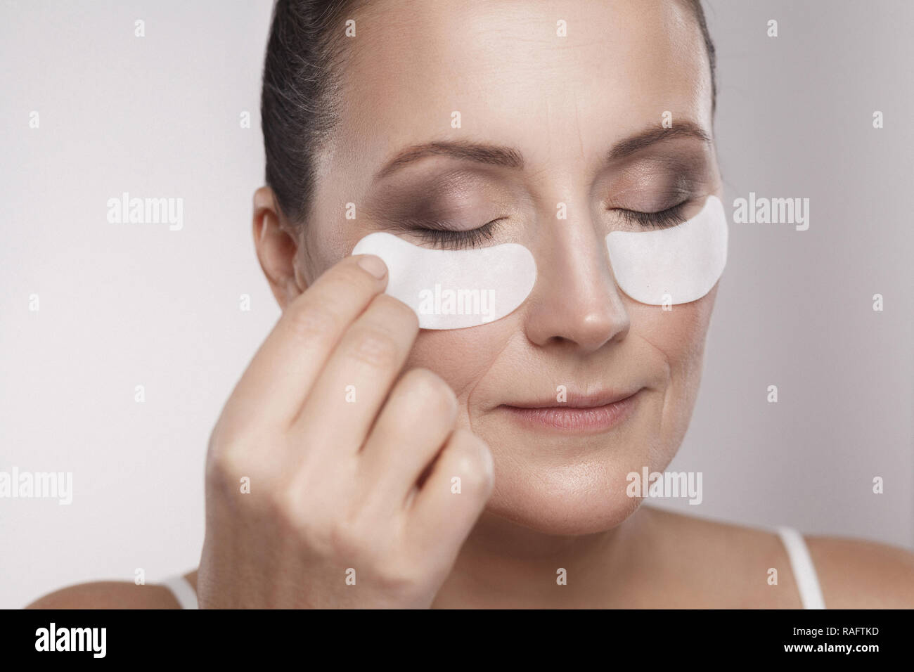 Closeup portrait de belle femme d'âge moyen avec une peau parfaite à l'aide de patchs hydrogel blanc de levage avec effet anti-rides le collagène, gray background Banque D'Images