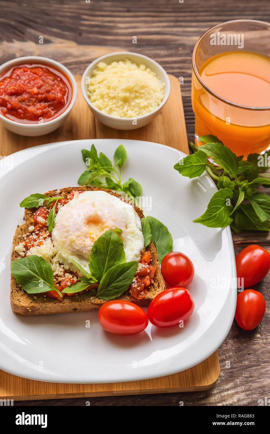 Petit-déjeuner des tartines avec oeuf poché, sauce tomate, basilic et parmesan sur fond de bois rustique Banque D'Images