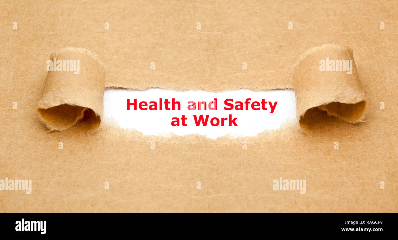 Texte La santé et la sécurité au travail qui apparaissent à travers un trou dans le papier marron déchiré. Banque D'Images