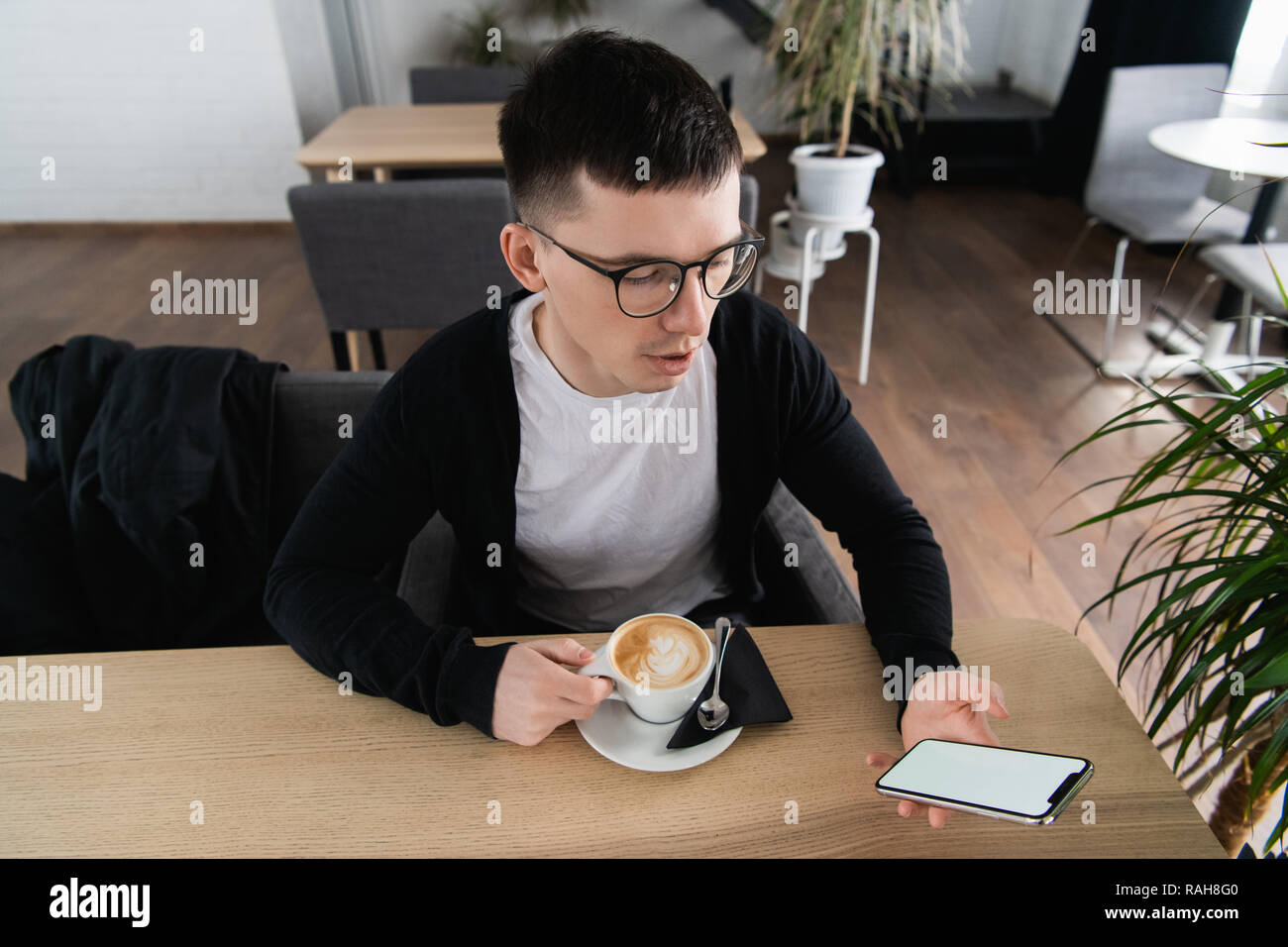 Young man holding mobile phone. Il est assis dans un restaurant ou un café. Il essaie de regarder une vidéo ou un film. Place pour votre publicité ou logo Banque D'Images