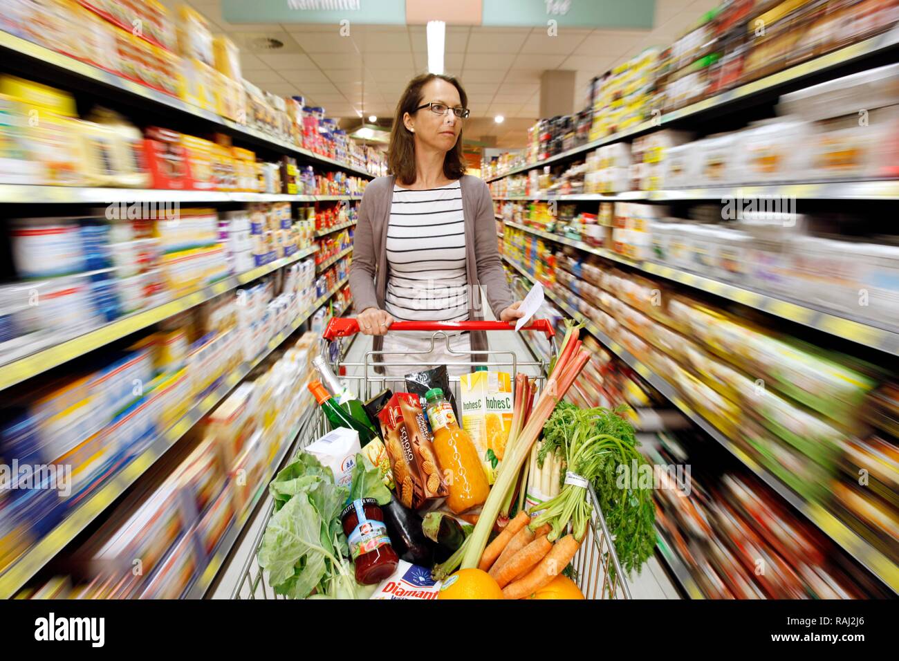 Woman un plein panier par un corridor de l'alimentation section tout en faisant des emplettes dans un ministère d'épicerie libre-service Banque D'Images