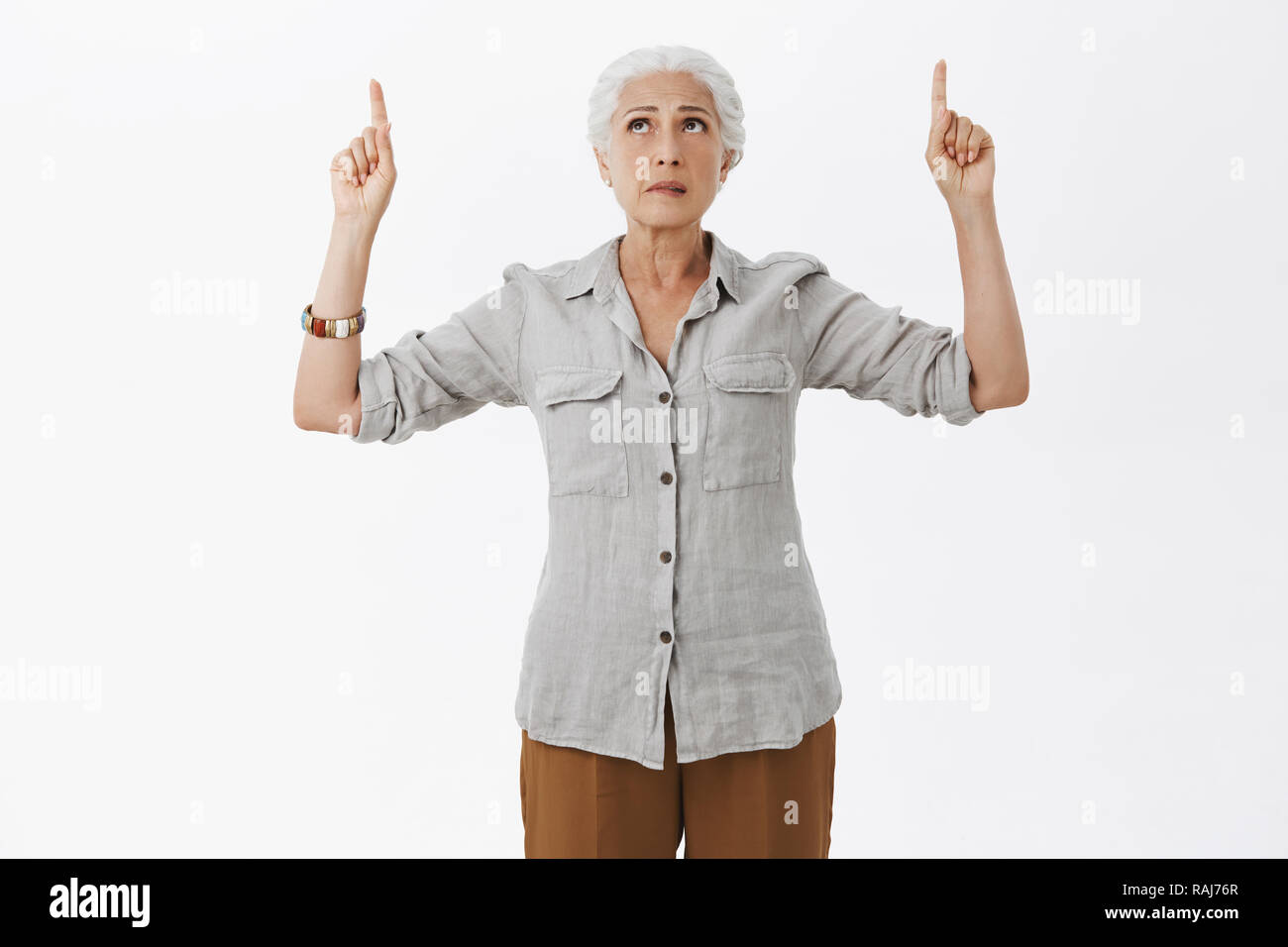 Studio shot of concernés hésitant et incertain perplexe vieille femme en chemise et pantalon à la pointe vers le haut et à l'expression inquiète pas certains des doutes qui posent sur fond gris Banque D'Images