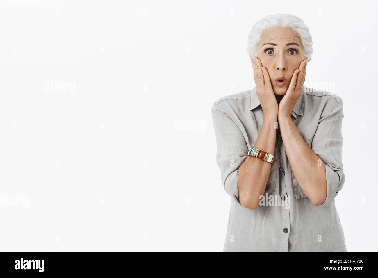 Portrait de surpris et choqué peur vieille dame aux cheveux blancs le pliage des lèvres et joues touchant de choc et stupeur se sentir nerveux réagissant à de terribles surprises, sur fond gris Banque D'Images