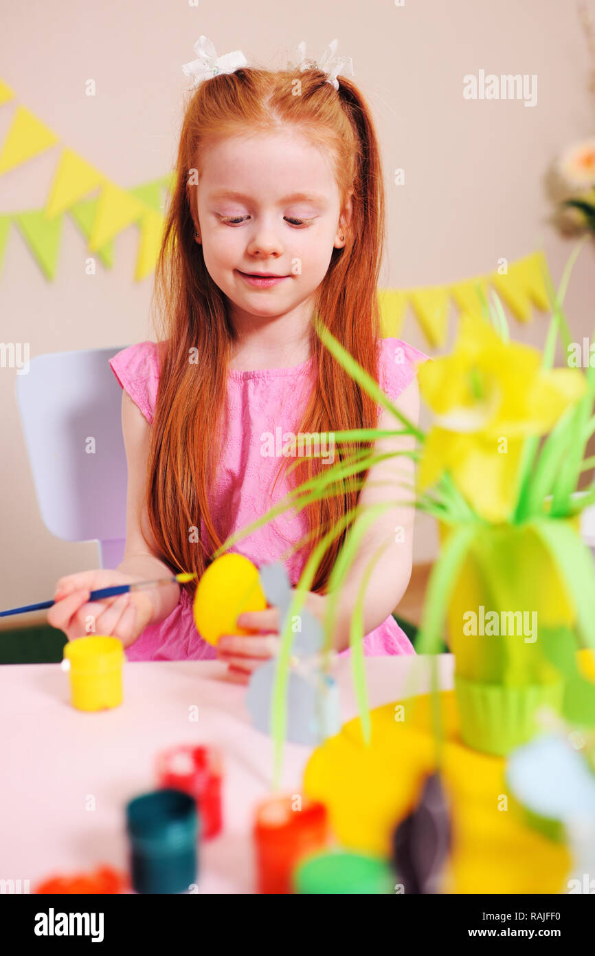 Petite fille aux cheveux rouges une coloration jaune d'oeuf sur le fond de la décoration de Pâques Banque D'Images