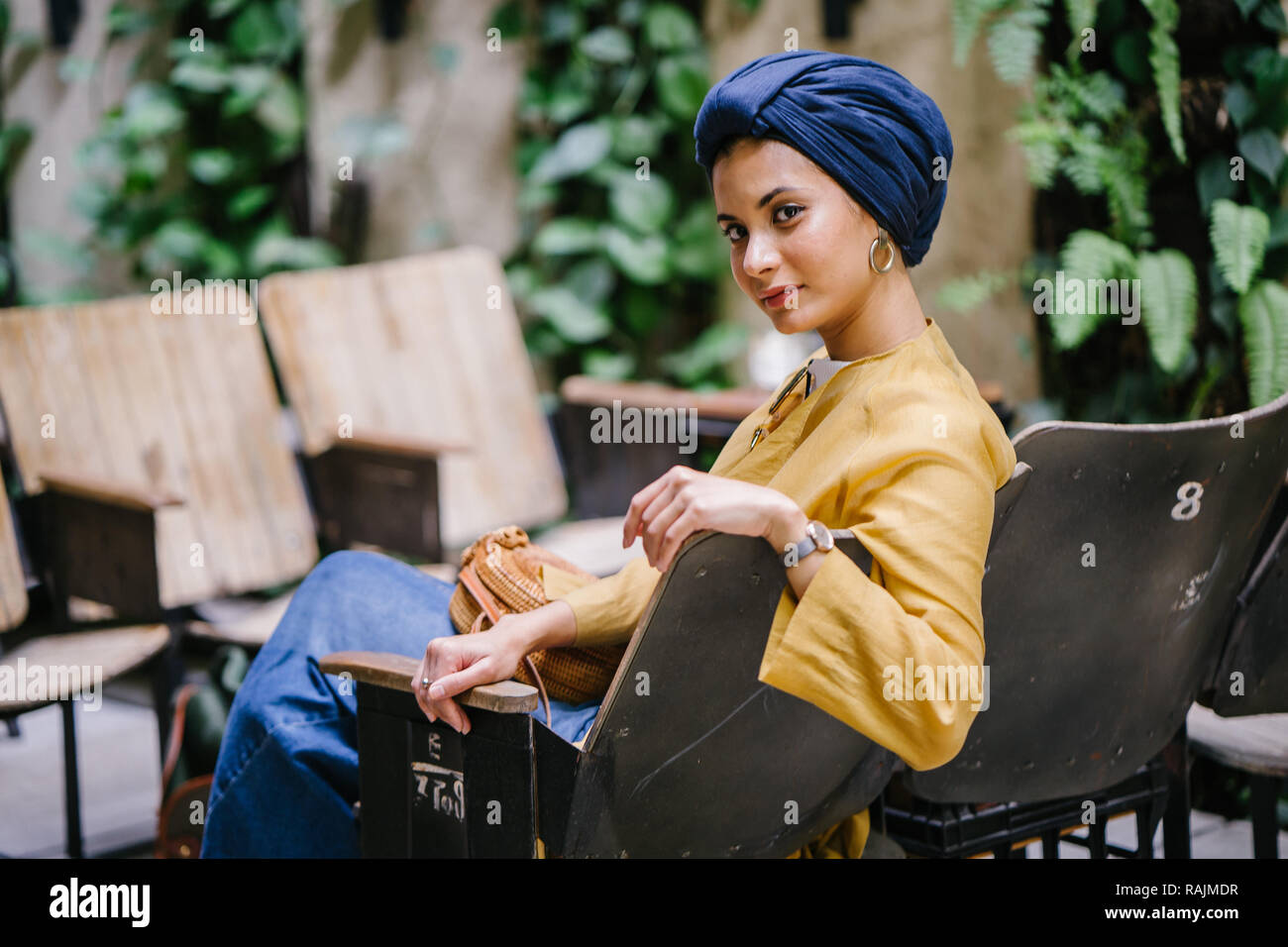 Une jeune femme du Moyen-Orient dans un turban hijab est assis et souriant dans un café dans la journée. Elle sourit joyeusement et est détendu. Banque D'Images