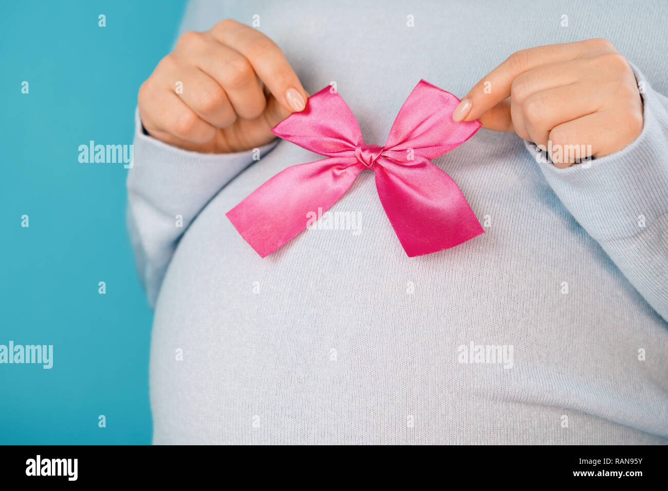 Pregnant woman holding noeud rose sur le ventre ventre arrière-plan. Jeune  fille attend bébé. La maternité, la grossesse, l'amour gratuit Photo Stock  - Alamy