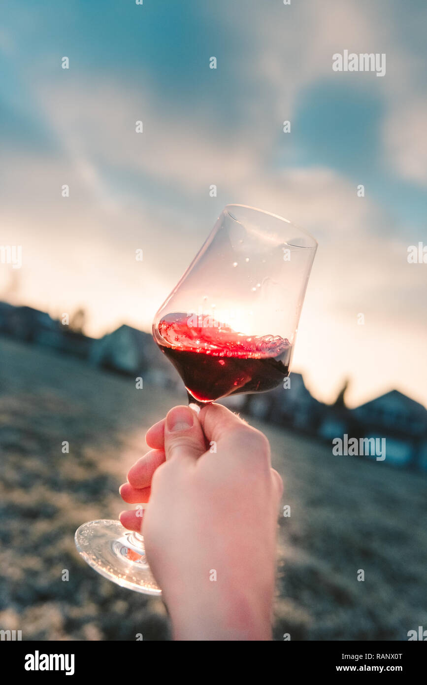 Point-de-View-Shot d'une main tenant un verre de vin rouge dans le soleil Banque D'Images