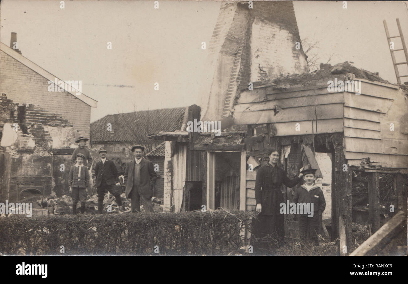 Vintage Carte postale photographique montrant un groupe de personnes édouardienne sur le site de l'incendie d'une maison. Un garçon vêtu d'un uniforme de marins. Banque D'Images