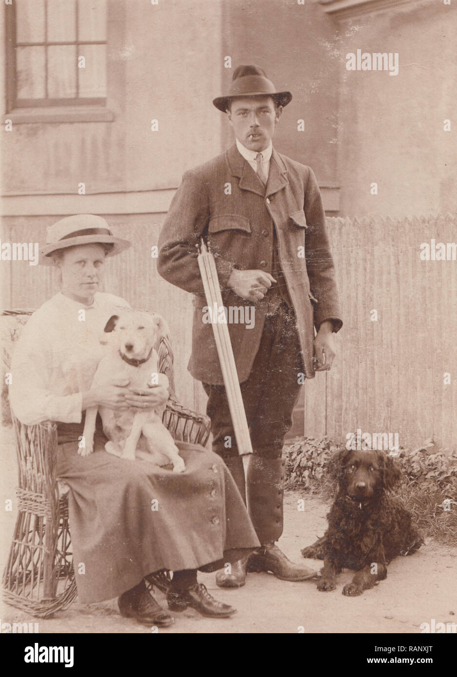 Vintage Carte postale photographique d'un mari et femme avec leurs deux chiens de compagnie. L'homme tient un fusil de chasse. Banque D'Images