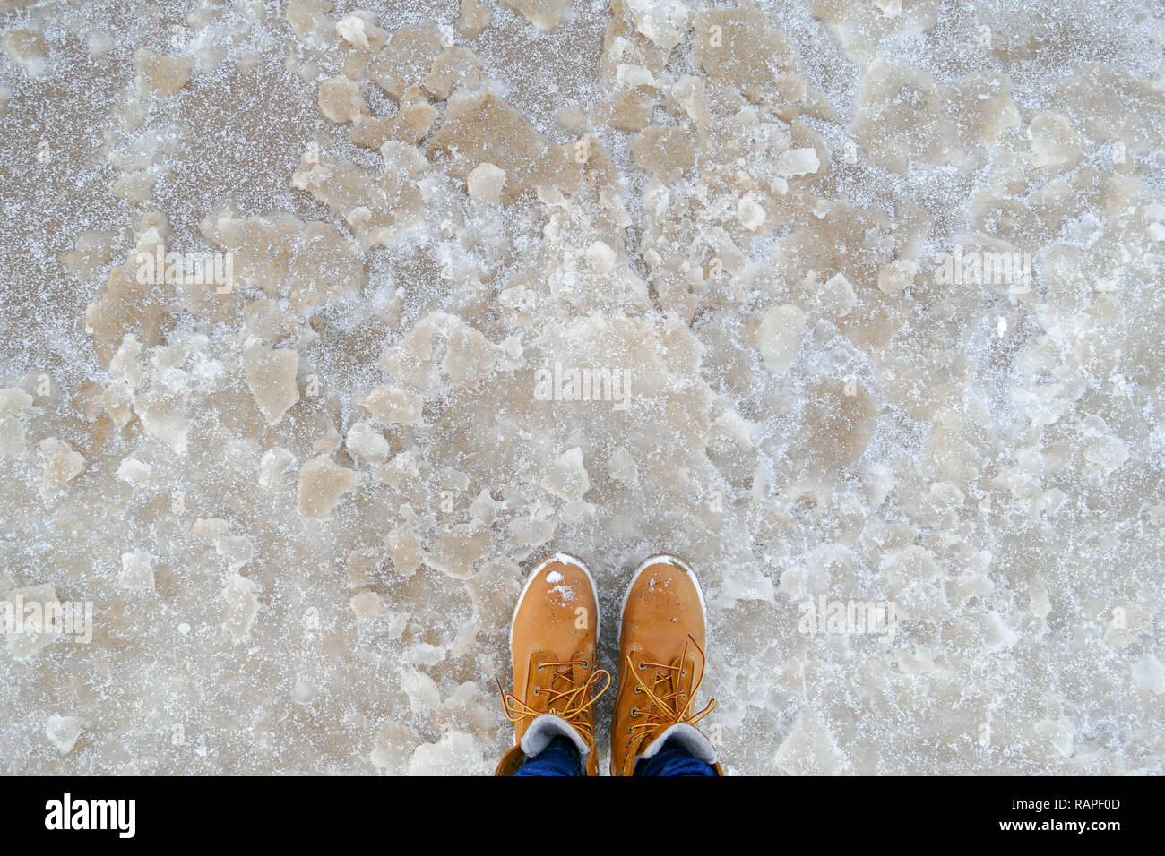 Vue de dessus de chaussures/bottes jaune debout sur la glace près de la mer. Saison d'hiver. Banque D'Images