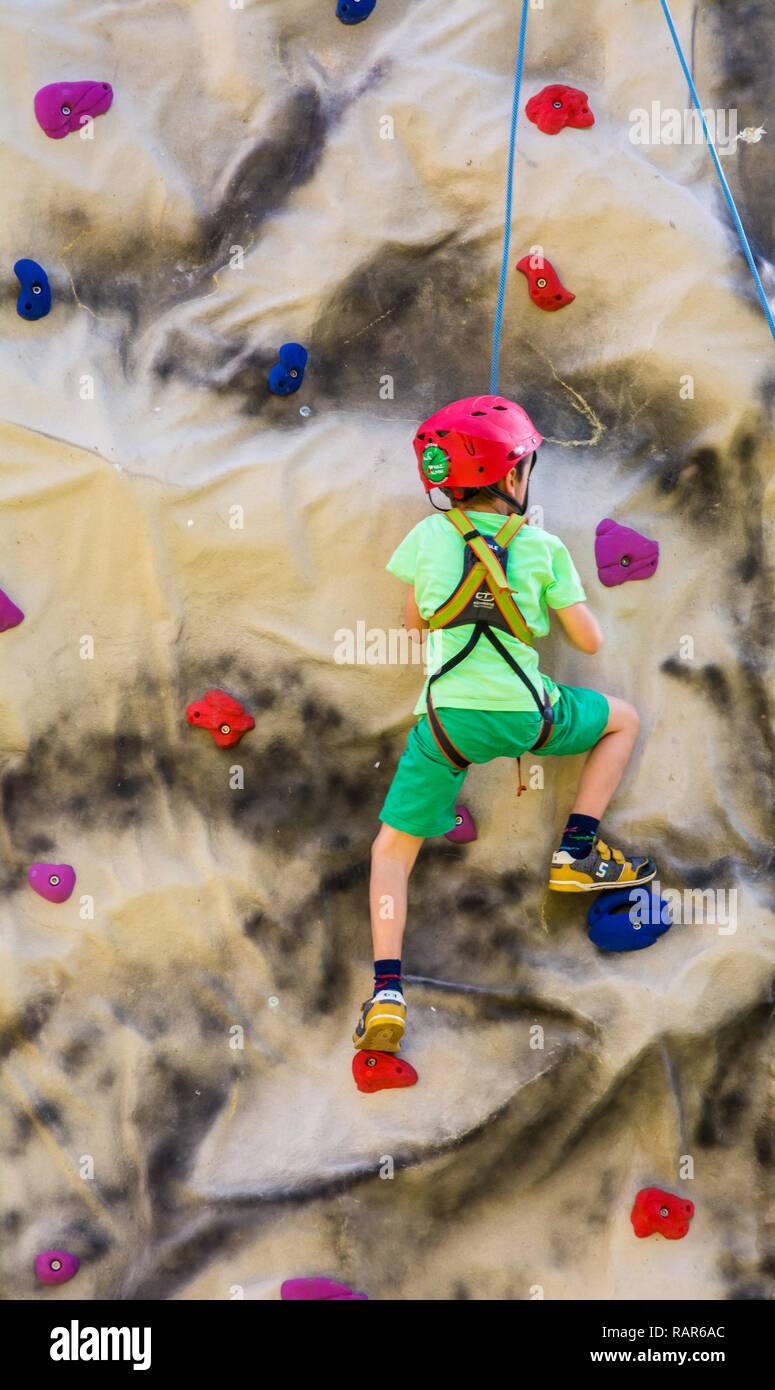 Photo de petit garçon dans un harnais escalade un mur avec poignées. Banque D'Images
