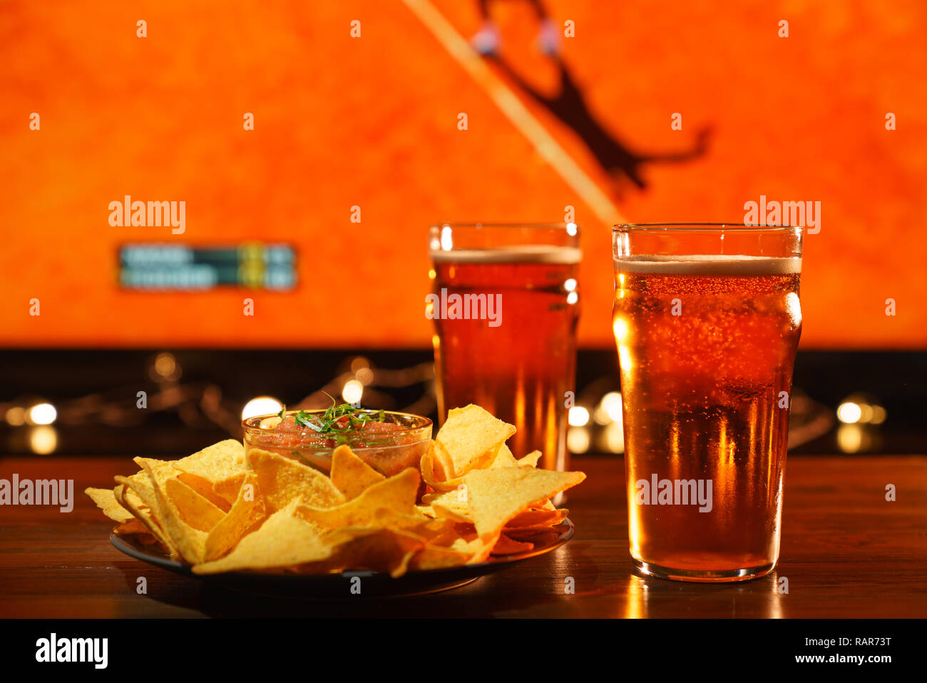 2 verres de bière avec des nachos et salsa sur une table en bois sombre. Sports bar, tennis sur un arrière-plan, la haute résolution Banque D'Images