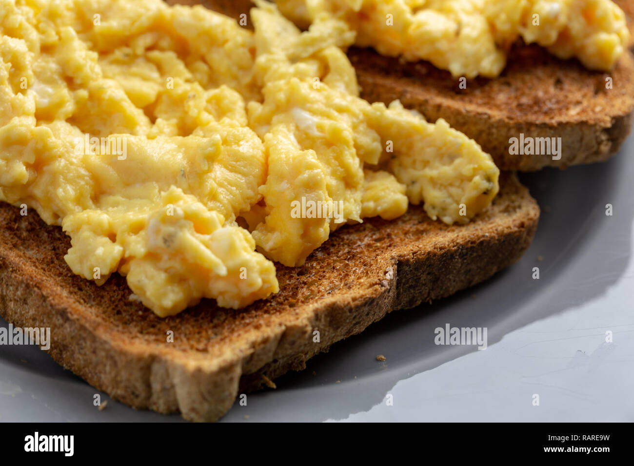 Close up d'œufs brouillés sur deux morceaux de pain grillé sur une plaque gris sur un simple fond marbré gris et blanc Banque D'Images