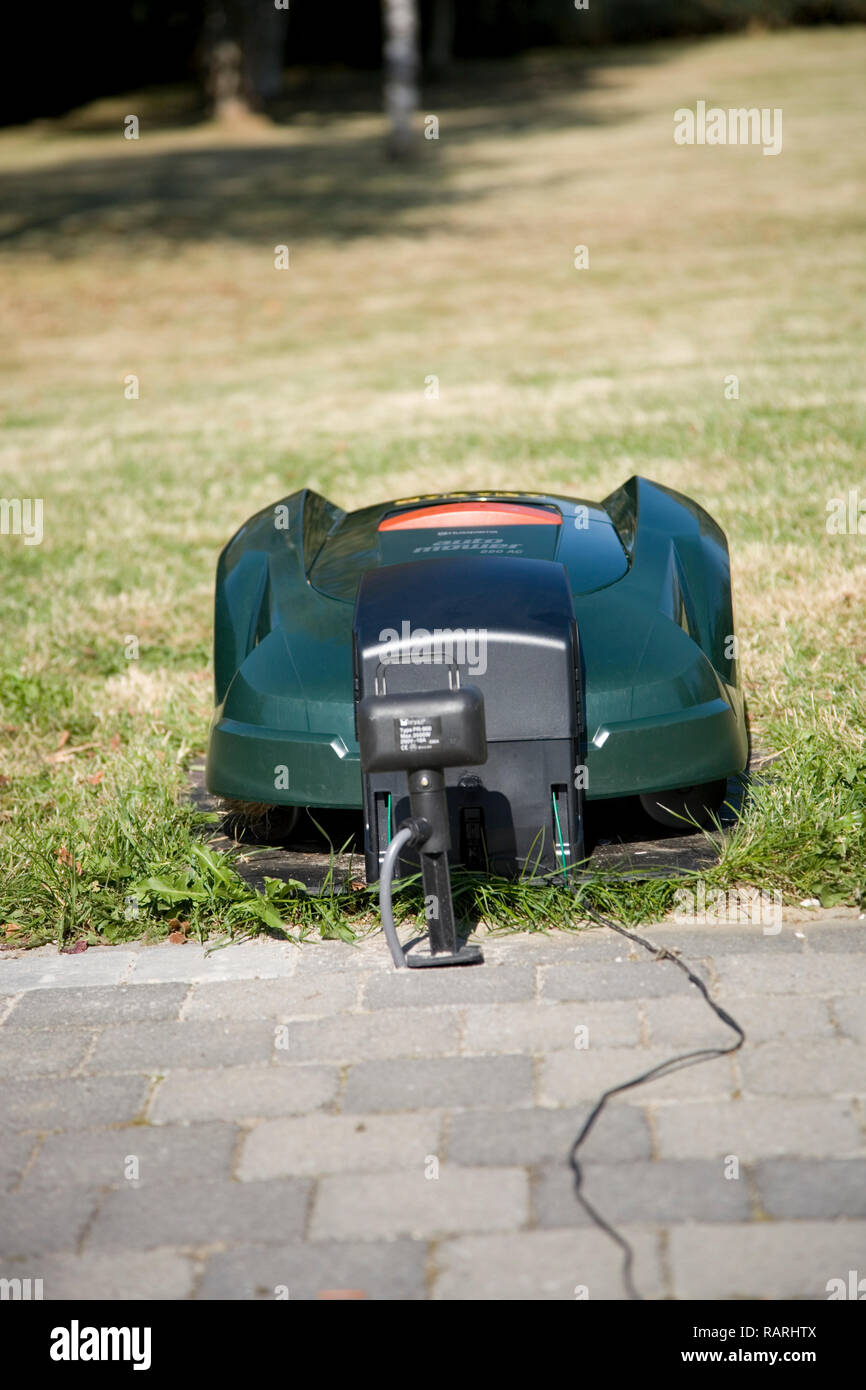Tondeuse robot automatique vert placé sur sa station de recharge à proximité d'un patio, vue de face à face Banque D'Images