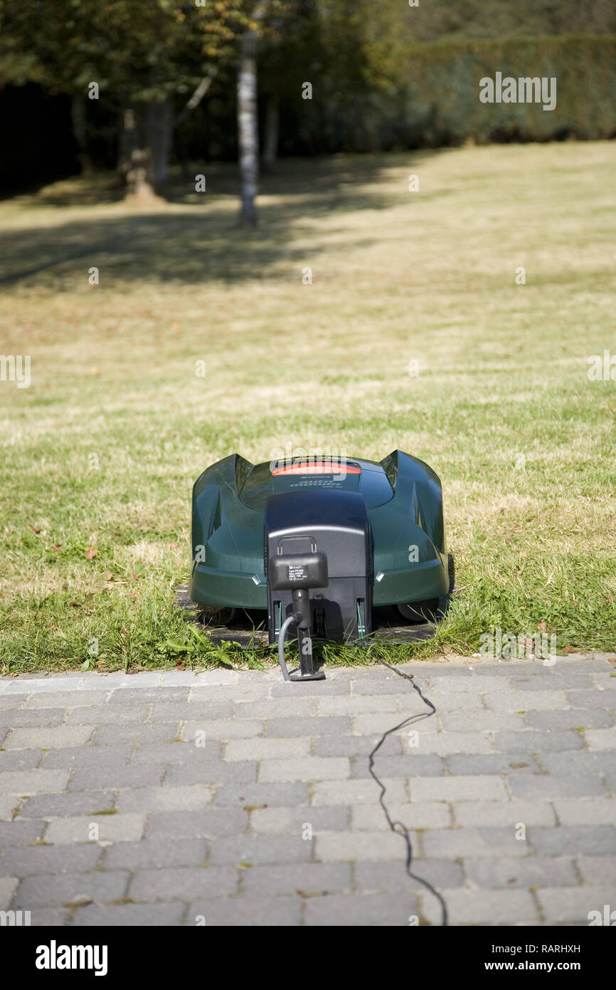 Tondeuse robot automatique vert placé sur sa station de recharge à proximité d'un patio, vue de face à face Banque D'Images