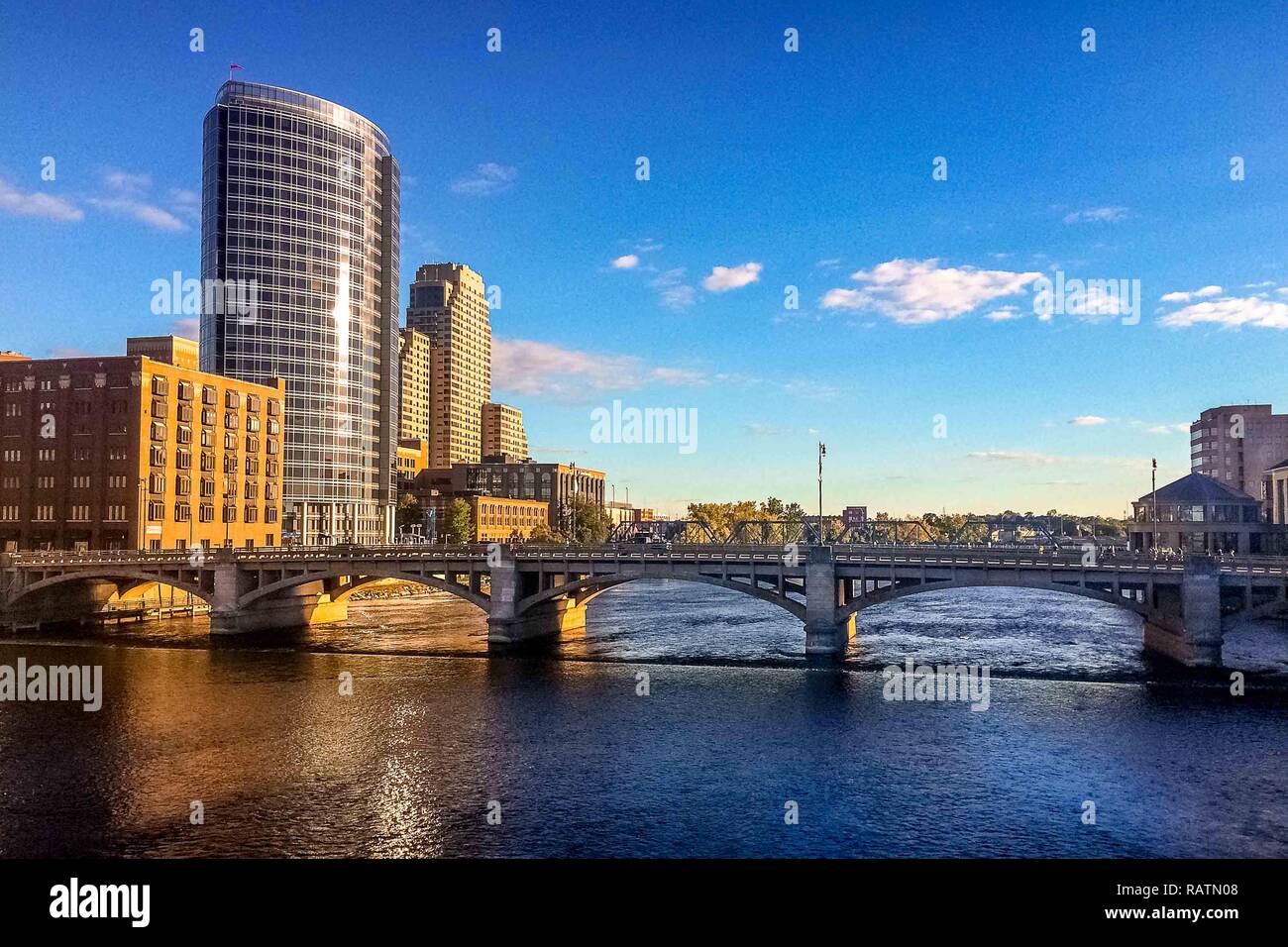 Heure d'or de la lumière du soleil reflétant le Grand Rapids, Michigan skyline avec ponts sur la rivière Grand et de barrage dans le premier plan avec un ciel clair. Banque D'Images