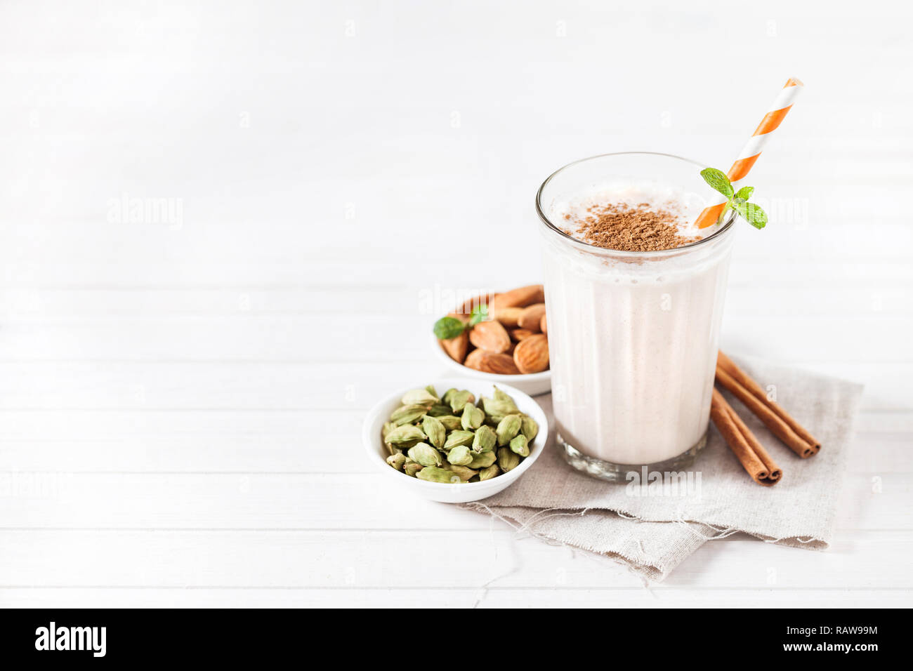 Amande caillé indien lassi aux épices cardamome et cannelle dans le verre avec stick à rayures sur fond blanc avec un espace réservé au texte Banque D'Images