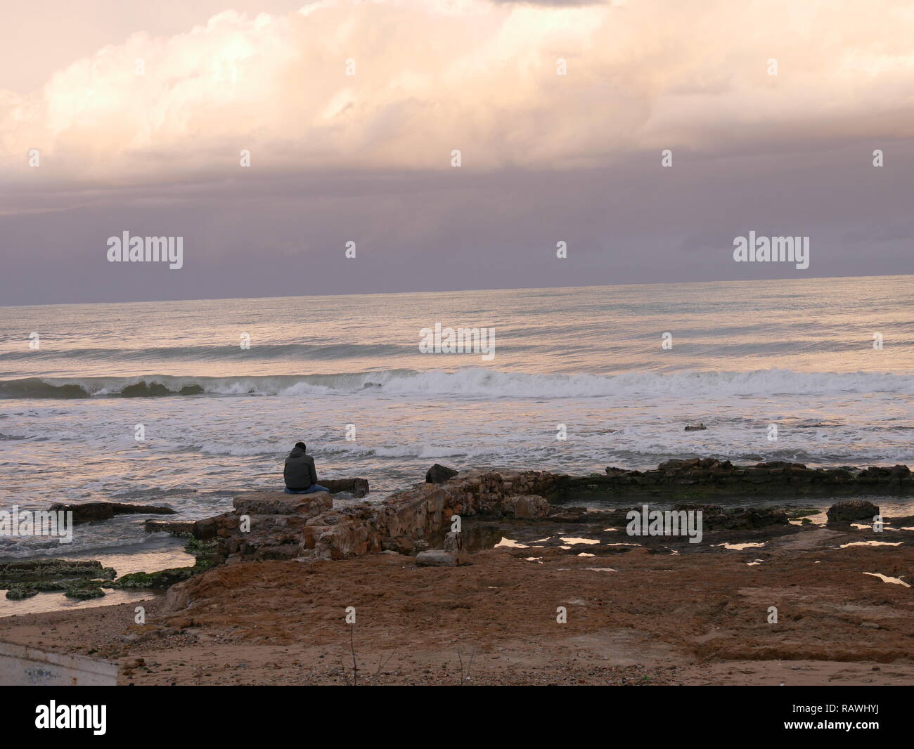 Homme assis sur une plage seul. Heure d'or, au cours d'une journée d'hiver, à gauche de Kobet El Haoua (Le Carré Blanc), Marsa plage, La Marsa, Tunis, Tunisie Banque D'Images